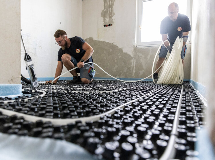 Zwei Mitarbeiter von Rieber installieren eine Fußbodenheizung in einem Rohbau