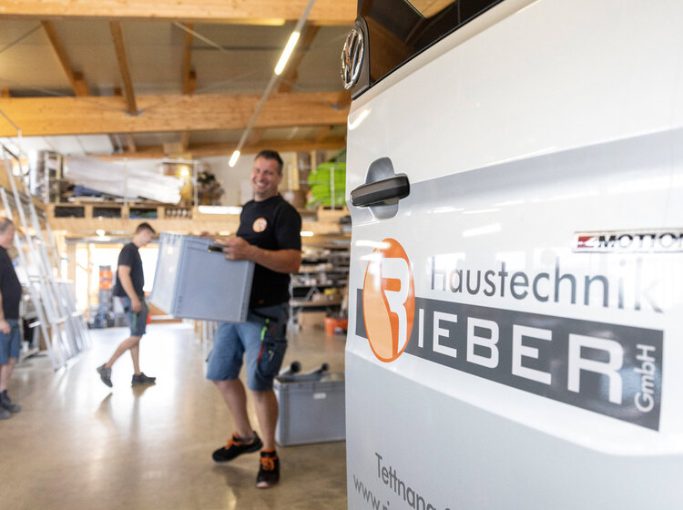 Mitarbeiter von Rieber Haustechnik beladen einen Firmenwagen im Lager